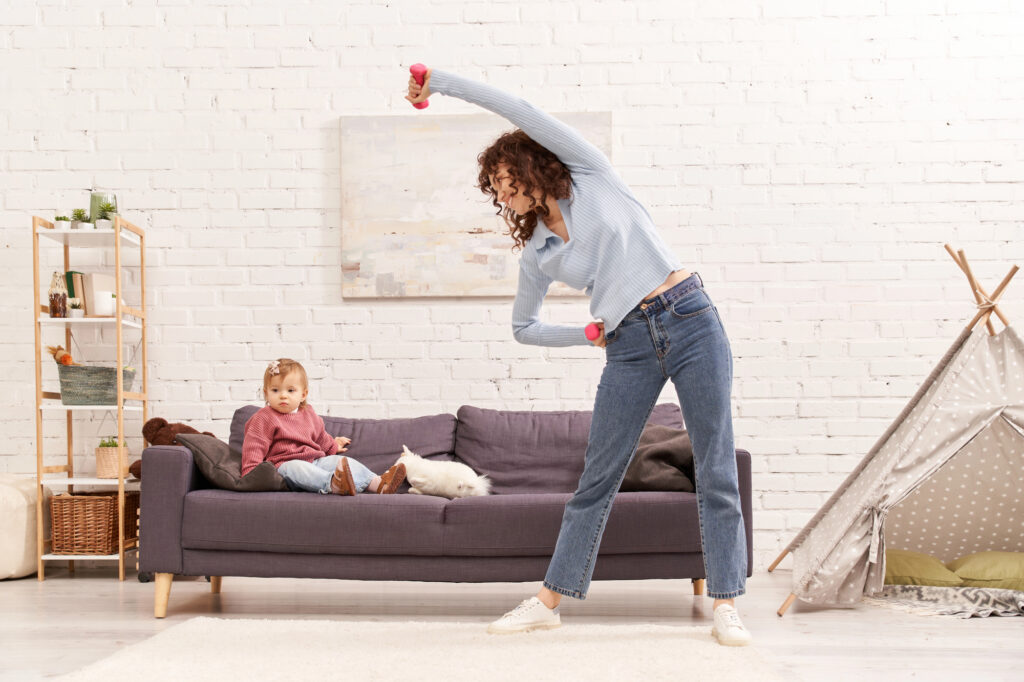 exercise for busy moms doesn't have to be complicated, image shows mom stretching with weights with toddler nearby on the couch