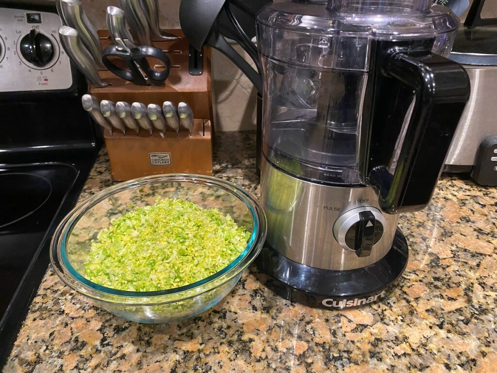 shredded brussels sprouts in a bowl next to food processor