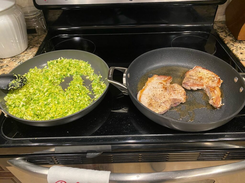 shredded brussels sprouts cooking in one skillet and juicy skillet pork chops cooking in another skillet