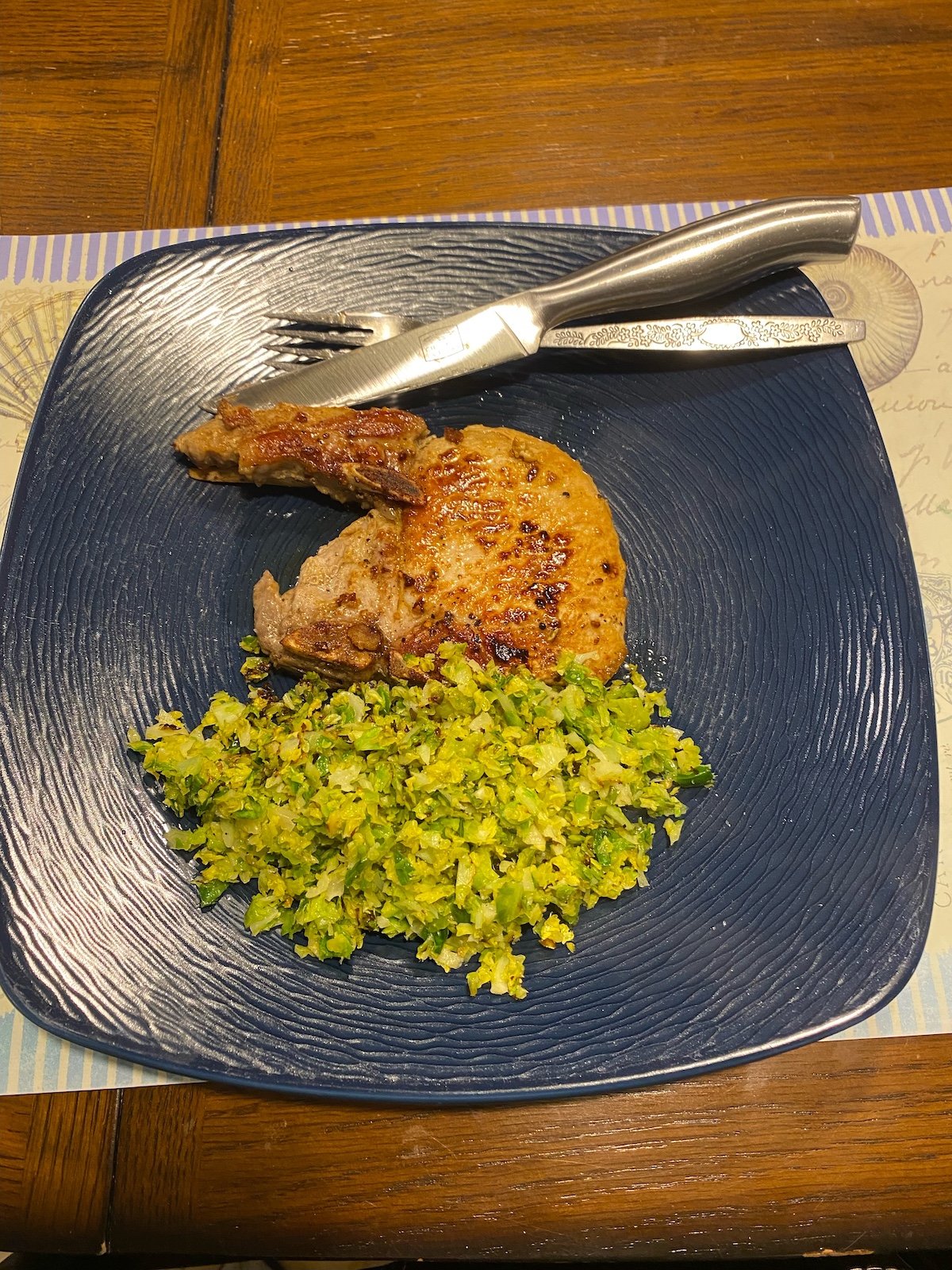 juicy skillet pork chops and shredded Brussels sprouts on dish with fork and knife