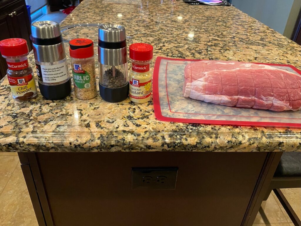image shows ingredients for slow cooker pulled pork shoulder bbq - chili powder, sea salt, minced garlic, black pepper, ground mustard, and pork roast