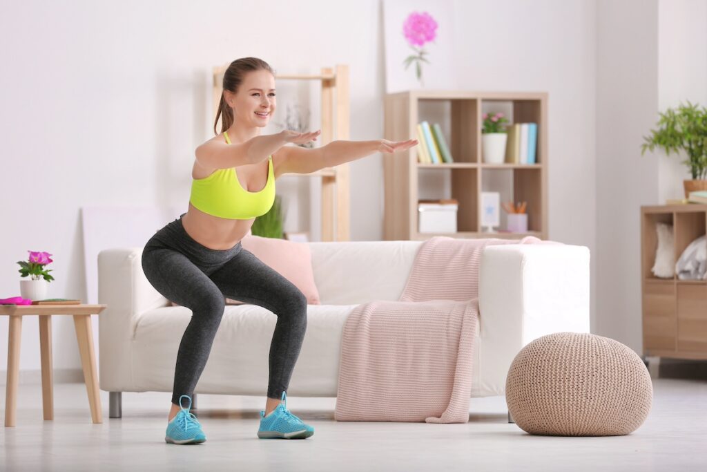 woman doing workouts for busy moms at home, holding a squat with arms raised