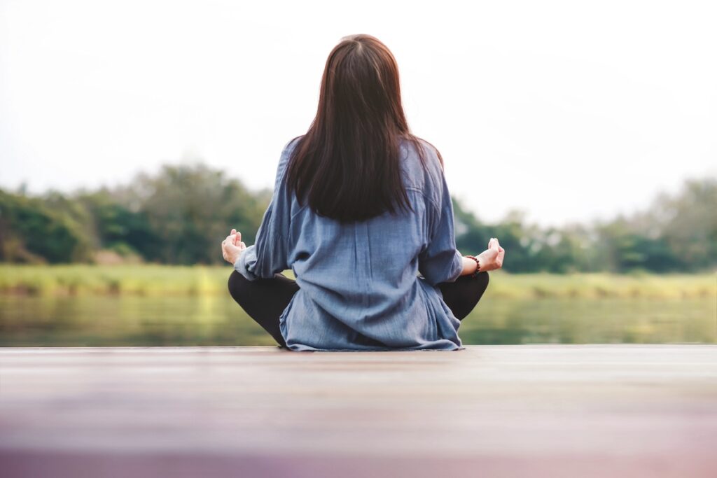 woman sitting outside and meditating, practicing easy wellness activities