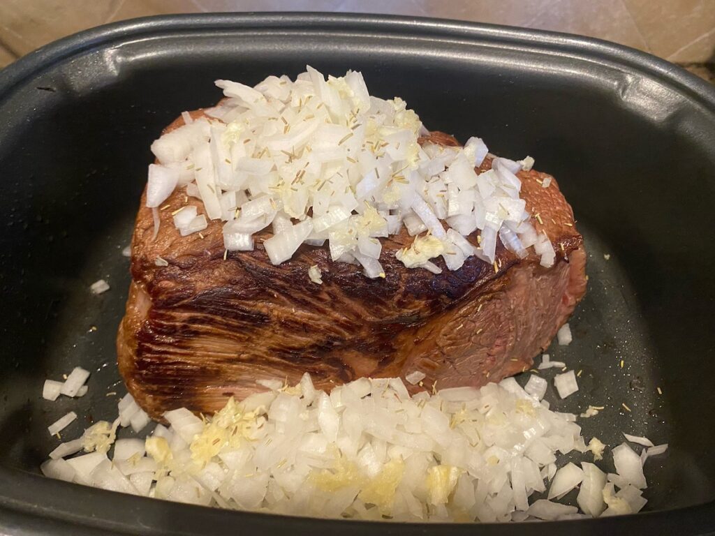 Italian pot roast in slow cooker with onions, garlic, and rosemary on top