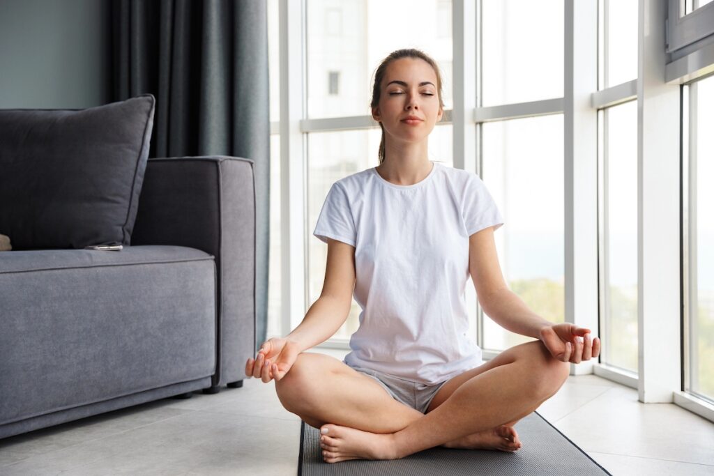 woman meditating at home near window, knows rest day benefits are important to health.
