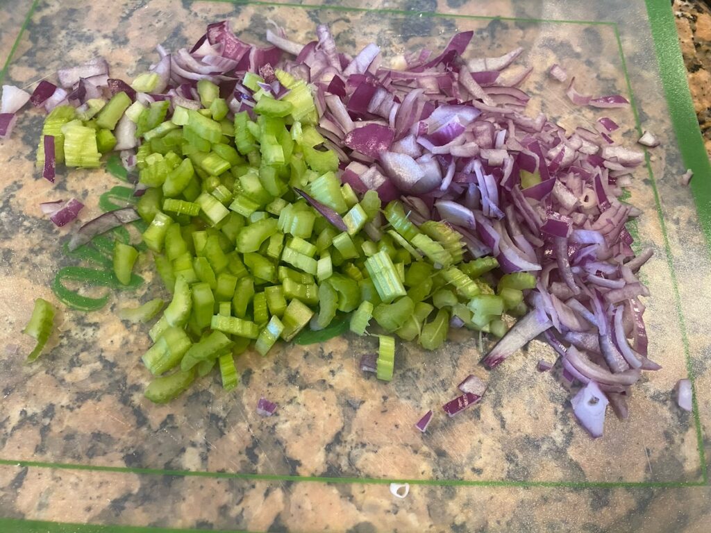 image shows celery and red onion finely chopped on cutting board