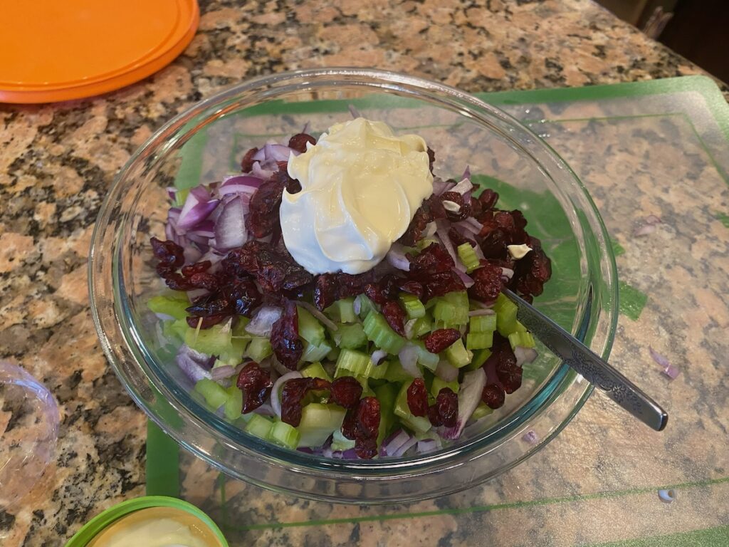 image shows cranberry tuna salad recipe ingredients - tuna, dried cranberries, celery, red onion, and mayonnaise - combined in a large bowl