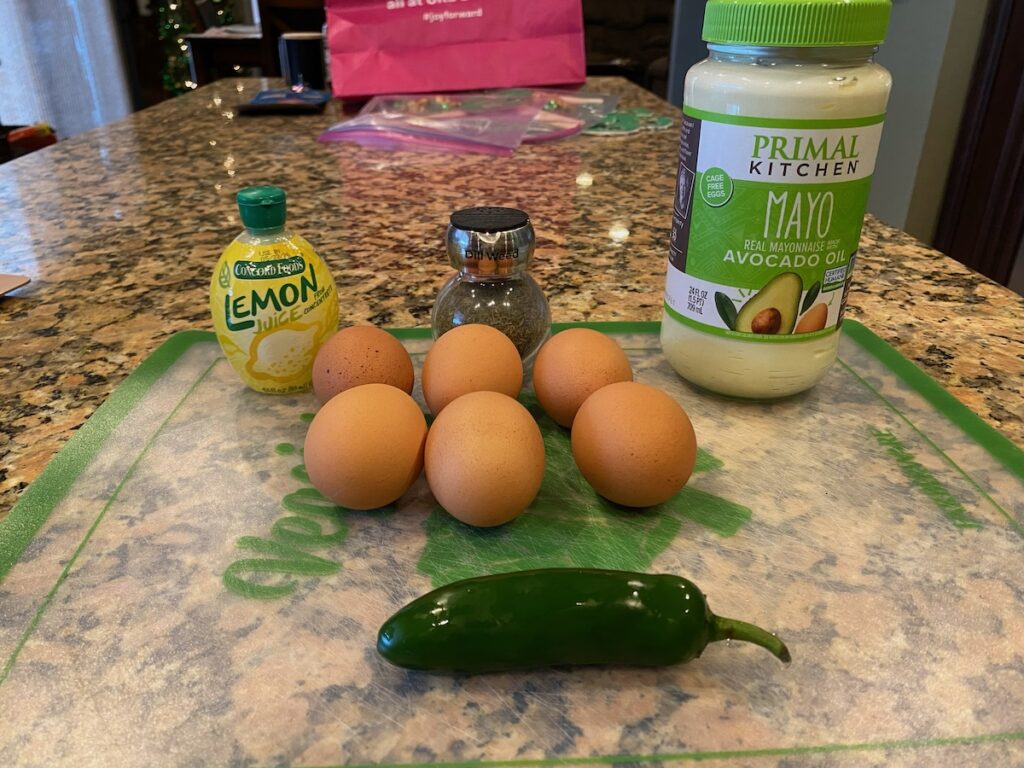 image shows ingredients for spicy egg salad recipe on cutting board on kitchen island - eggs, jalapeño pepper, mayonnaise, lemon juice, and dried dill weed