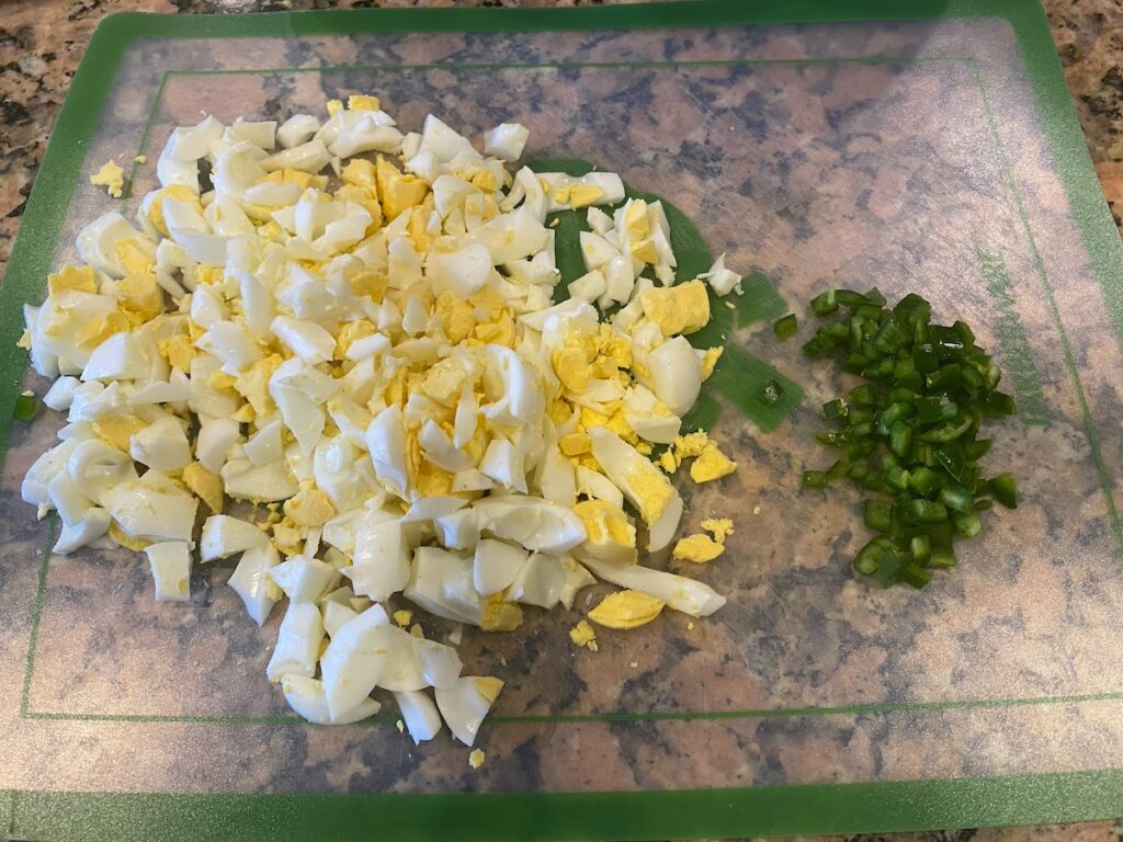 image shows ingredients for spicy egg salad recipe - boiled eggs and jalapeño pepper - after chopping step