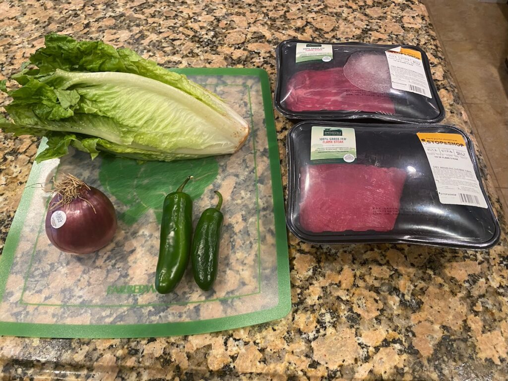 ingredients for healthy steak salad recipe - romaine lettuce, red onion, jalapeño pepper, and steaks - shown on kitchen island