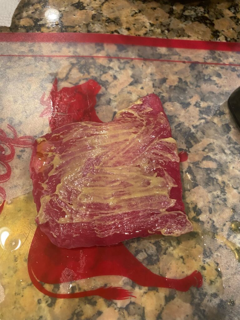 image shows raw steak smeared with mustard and olive oil, ready for cooking for the healthy steak salad recipe