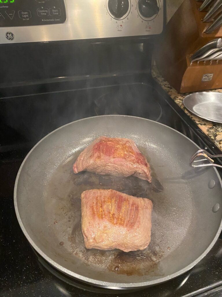 image shows steak seared in a pan on the stove
