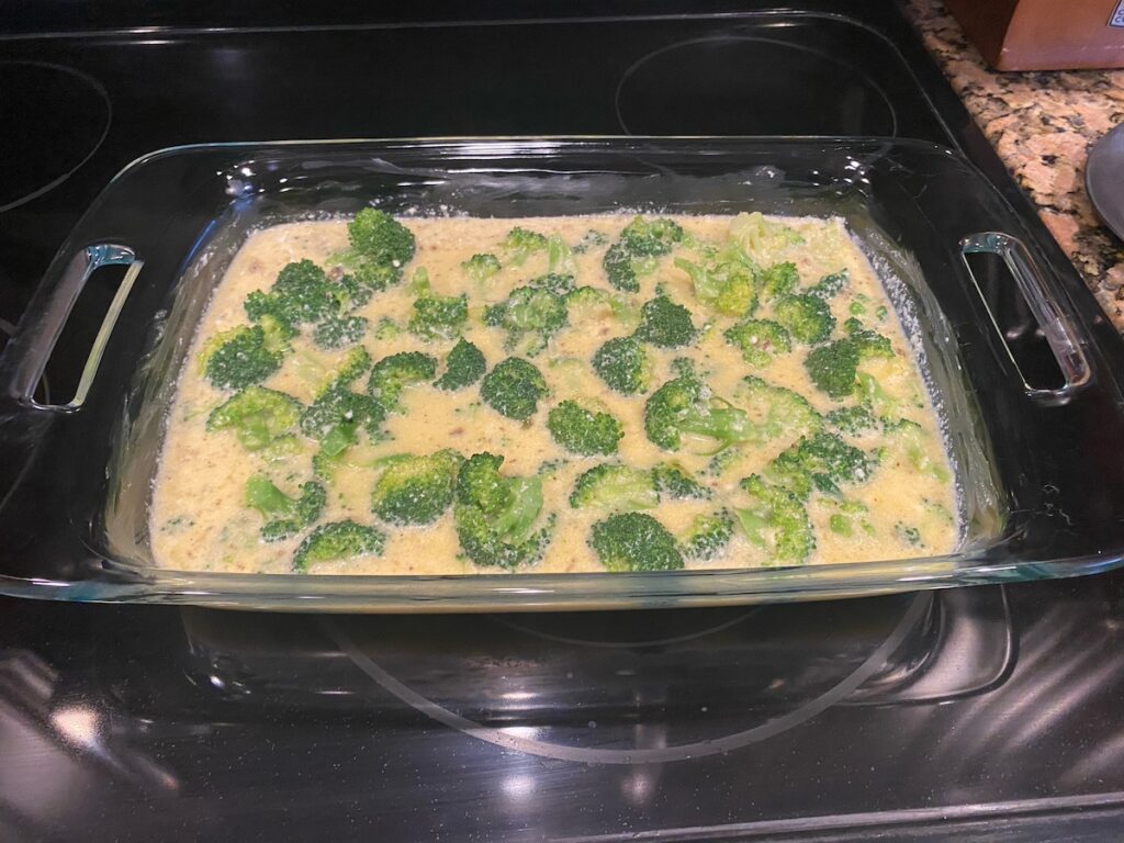 image shows all the ingredients for crustless broccoli quiche in baking dish ready to go in the oven