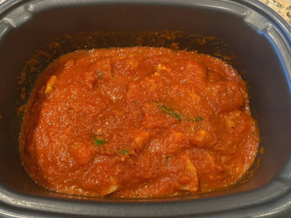 image shows chicken covered by marinara sauce in the slow cooker