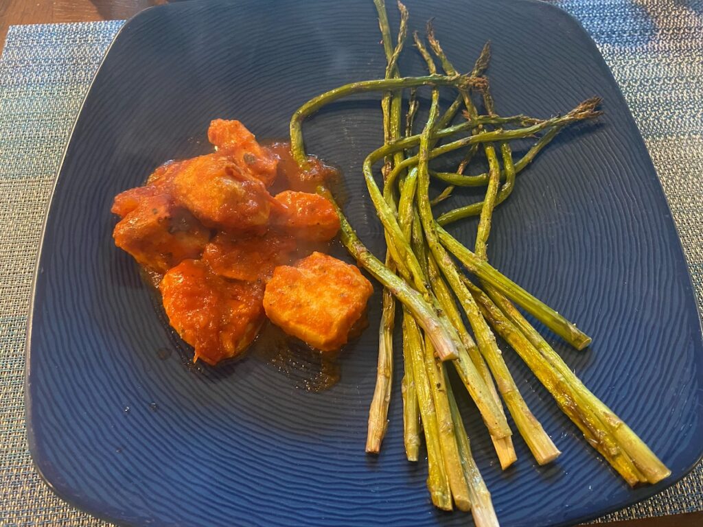 image shows cooked slow cooker Italian chicken with roasted asparagus on dinner plate