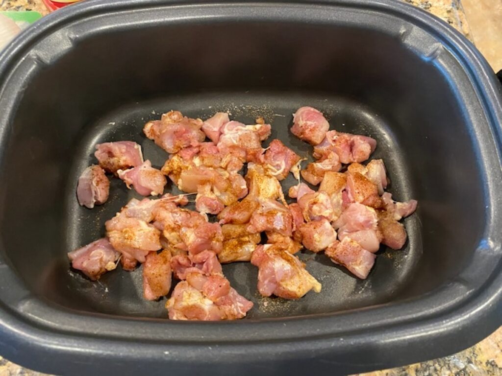 image shows raw chicken in slow cooker coated in spices