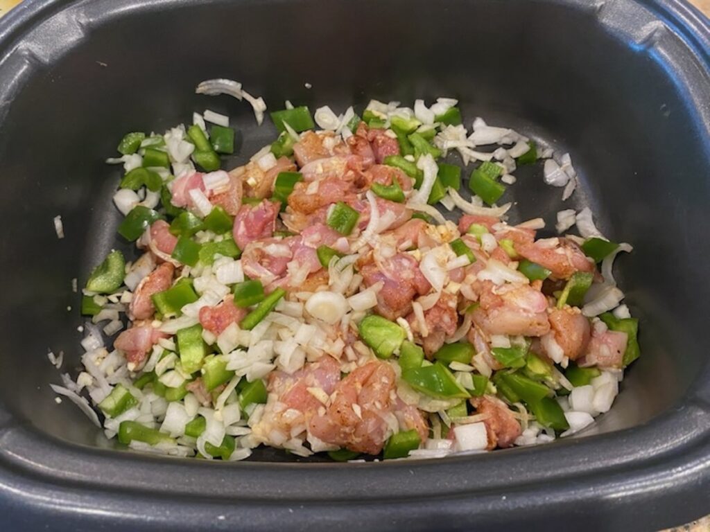 image shows chicken and vegetables in slow cooker mixed together