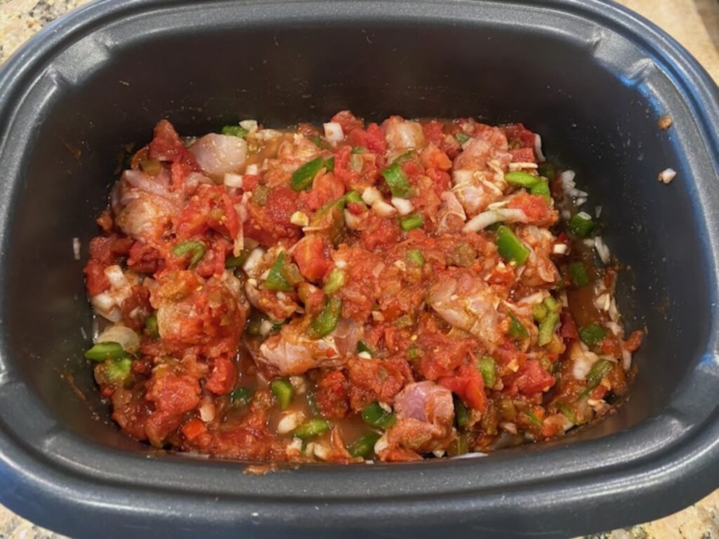 image shows chicken, vegetables, and tomatoes all mixed together in the slow cooker