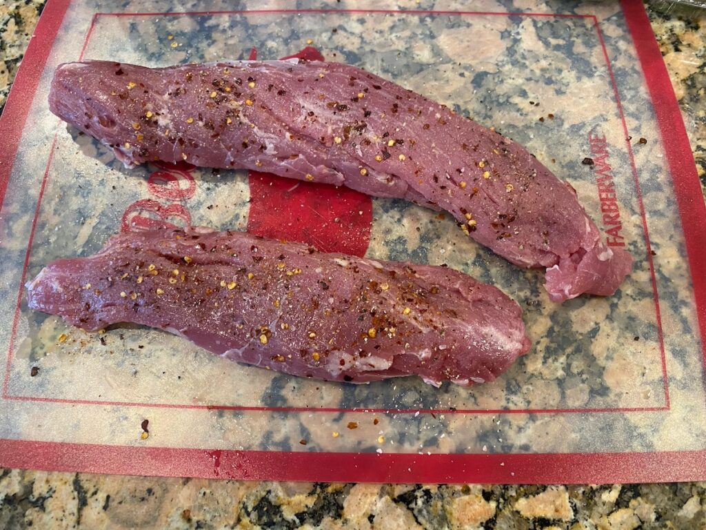 image shows pork tenderloin on cutting board covered in spices
