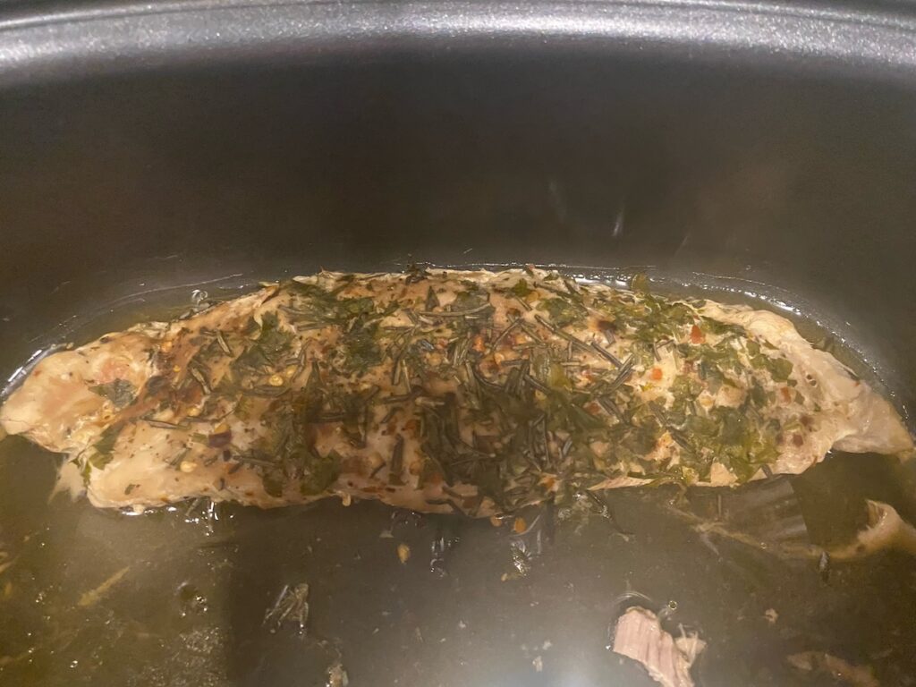 image shows fully cooked slow cooker herbed pork tenderloin in the slow cooker