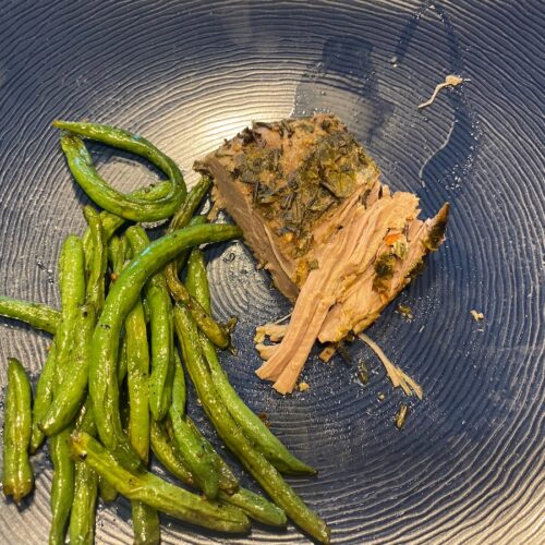 image shows slow cooker herbed pork roast on dinner plate with roasted string beans
