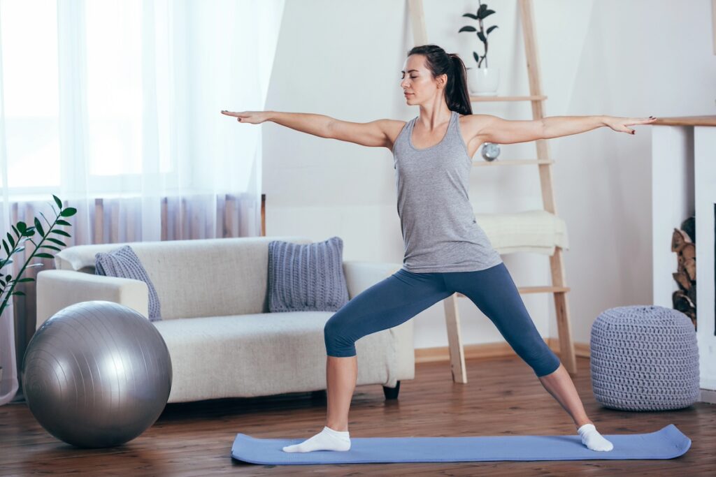 image shows woman practicing yoga in her living room, one of the low-impact workouts for moms