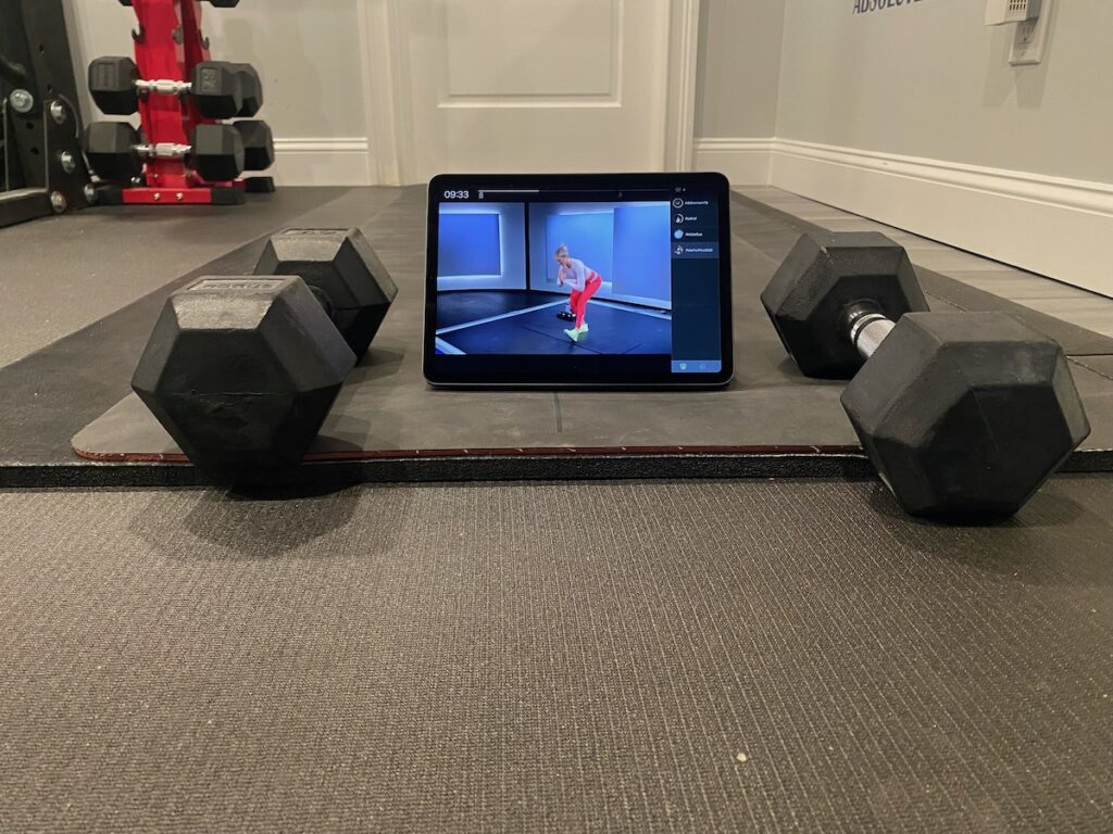 image shows Peloton app being used on iPad in between dumbbells