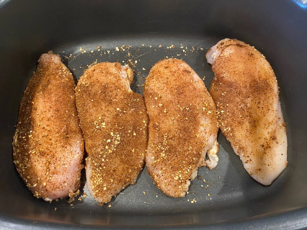 image shows chicken breasts in slow cooker covered in spice rub