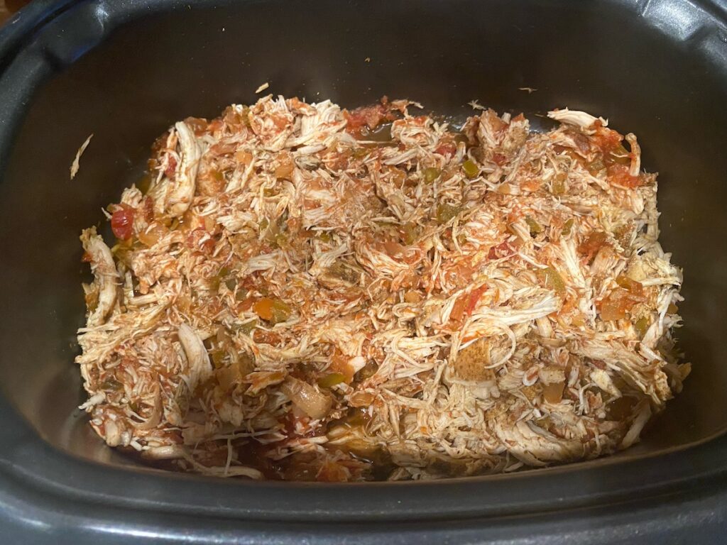 image shows shredded chicken mixed with salsa in the slow cooker