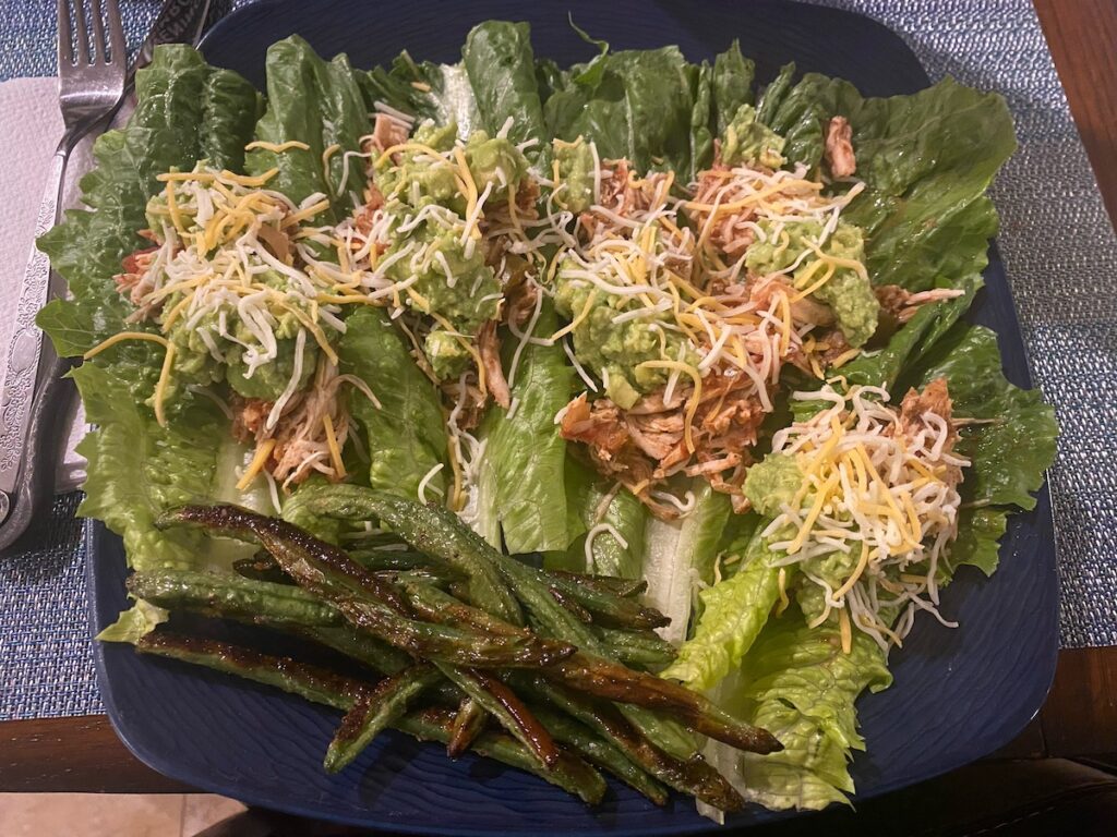 image shows healthy slow cooker chicken tacos as lettuce wraps, topped with guacamole and shredded cheese on a dinner plate