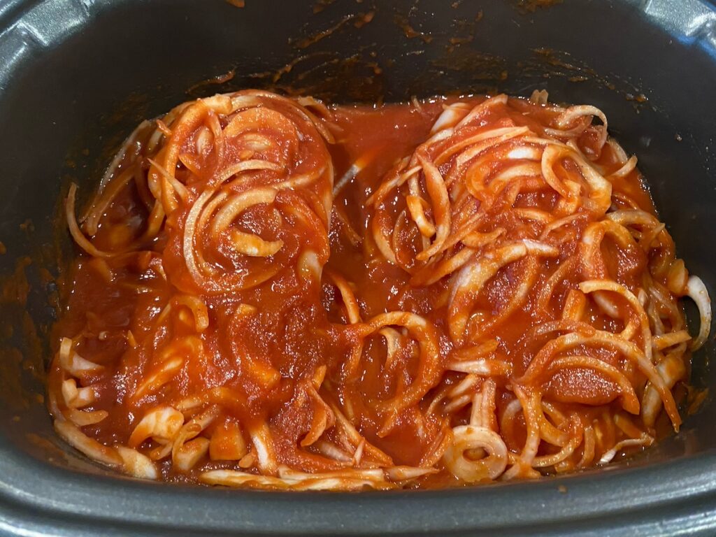image shows chicken in slow cooker covered by tomato sauce mixture