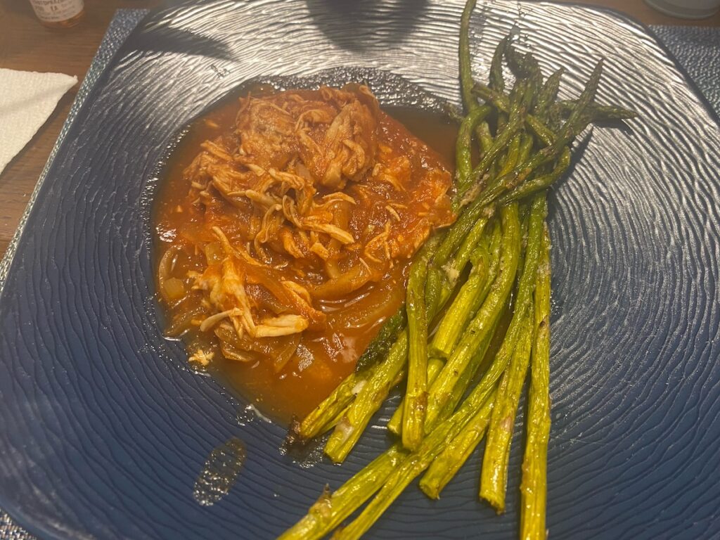 image shows slow cooker enchilada chicken on blue dinner plate with roasted asparagus
