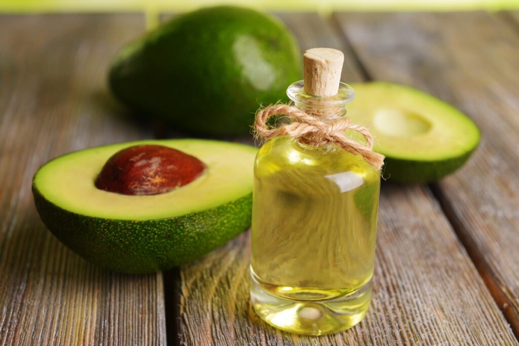 image shows avocados and jar of avocado oil on table