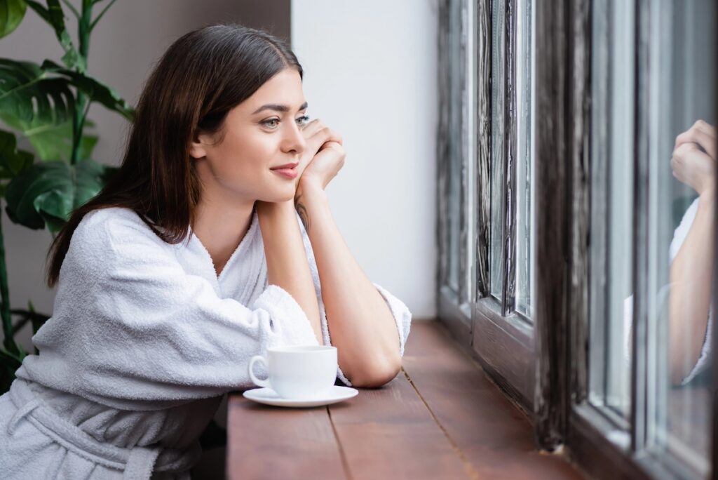 woman having a mindful moment, gazing out the window, practicing self-compassion