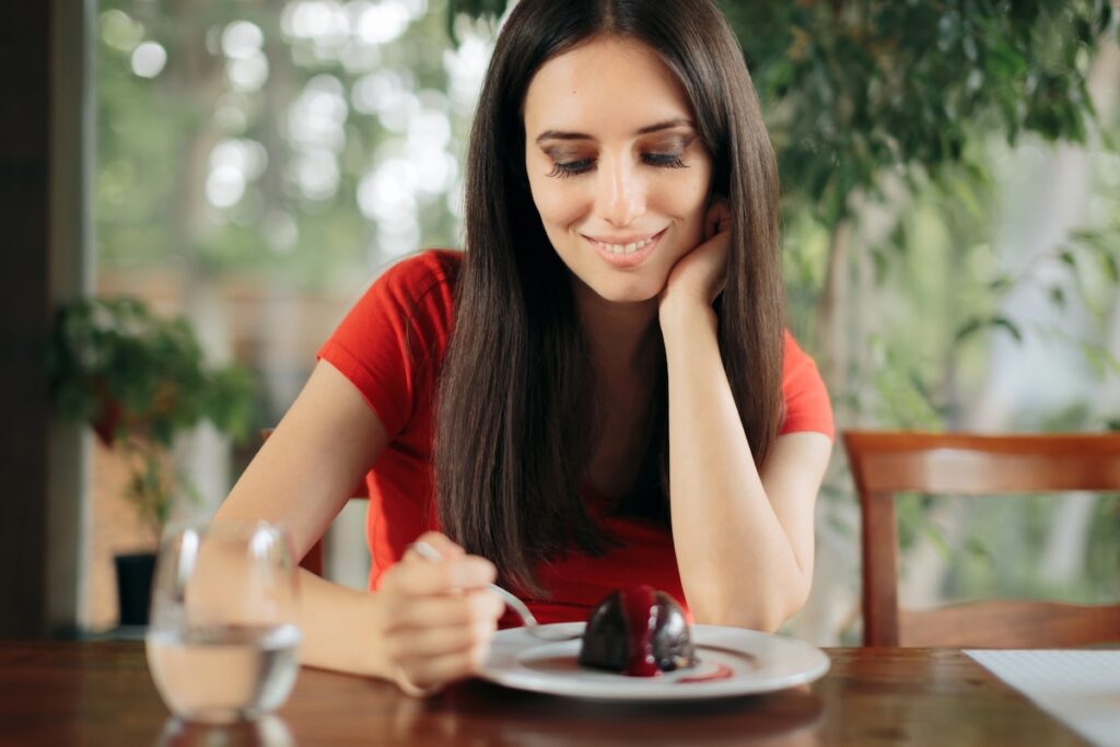Woman in her 40s eating small chocolate treat instead of cutting sugar to lose weight